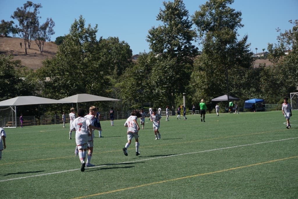 Youth players in white and red kits compete on a sunny turf field